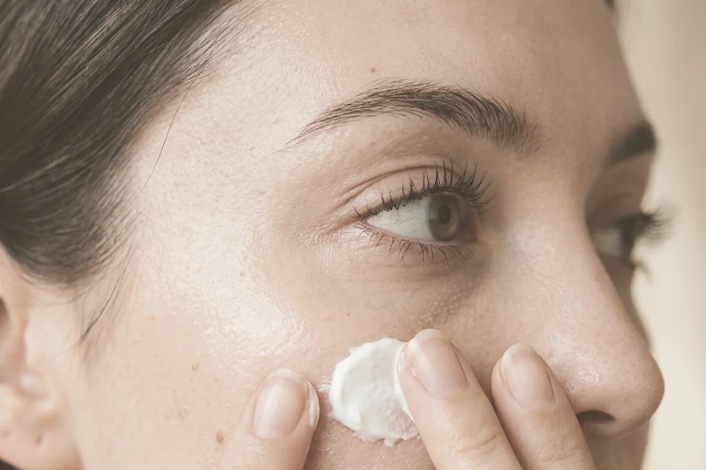 Creme sendo aplicado na bochecha com a ponta dos dedos